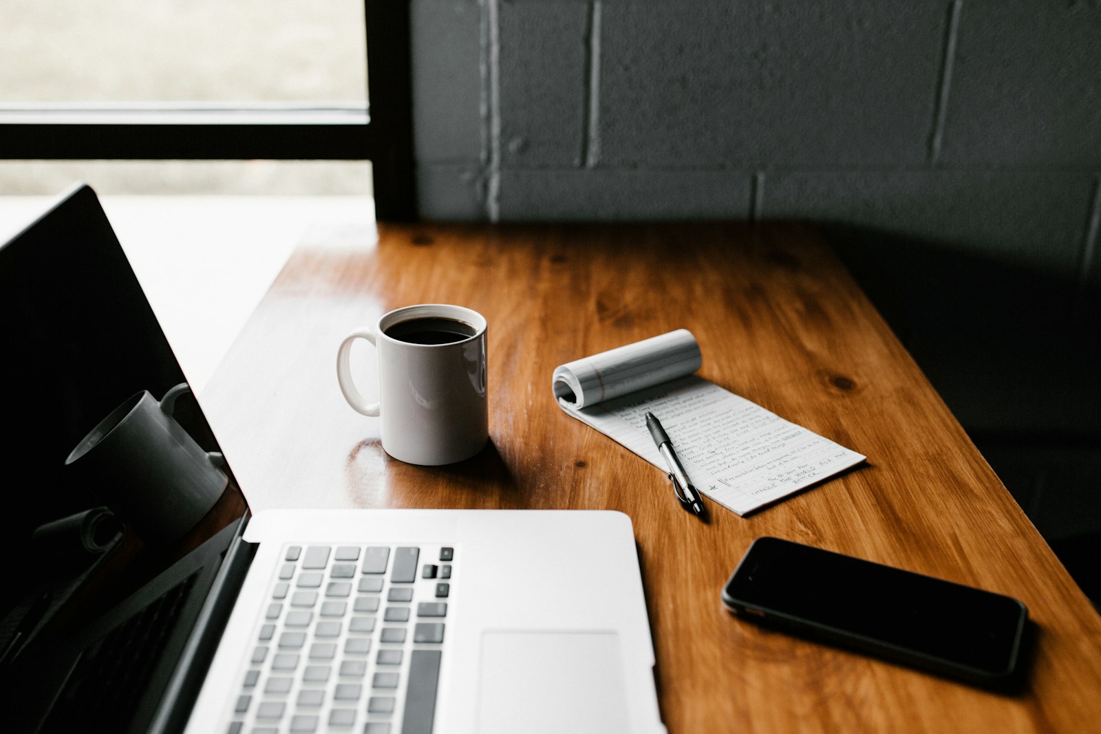 A writing desk with a laptop, notebook, and everyday tools